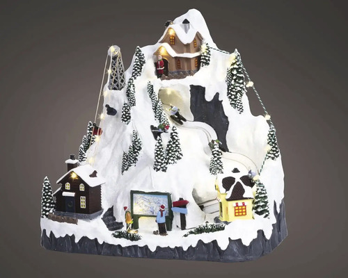 Vianočná miniatúrna zimná krajina so zasneženou horou, osvetlenými domami, lyžiarmi a lanovkou.