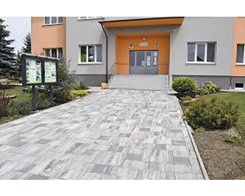 Moderný chodník zo sivo tieňovanej dlažby vedúci k domovému vchodu, obklopený zelenými krami.