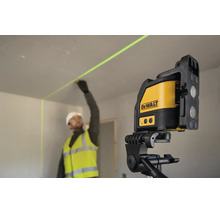 Stavebný robotník v pracovnom odeve označuje stenu pomocou krížového lasera DeWalt na statíve v interiéri.