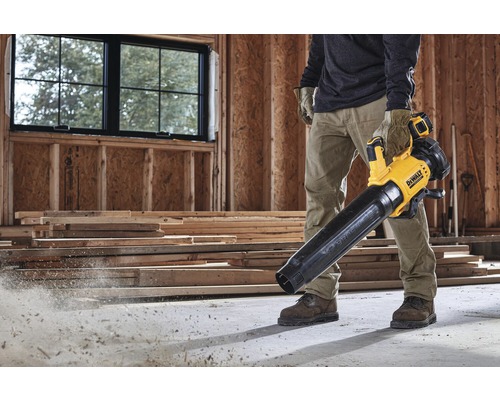 Muž používa žltý a čierny akumulátorový fúkač lístia DeWalt na stavenisku.