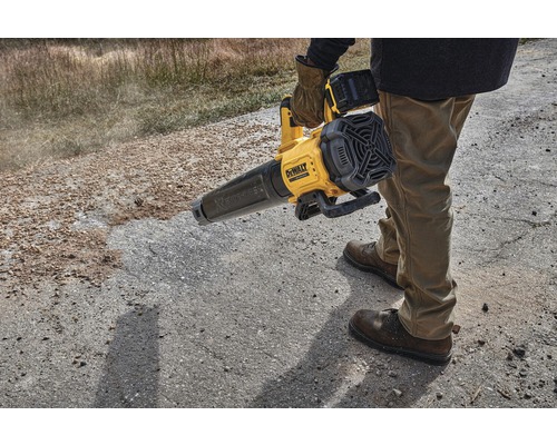 Osoba obsluhuje žltý akumulátorový fúkač lístia DeWalt na nespevnenom povrchu.