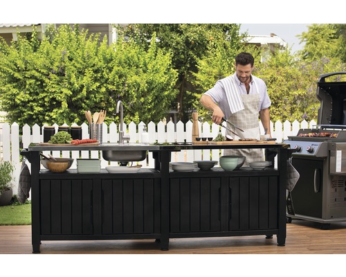 Vonkajšia kuchyňa s drezom, grilom a osobou, ktorá pripravuje jedlo