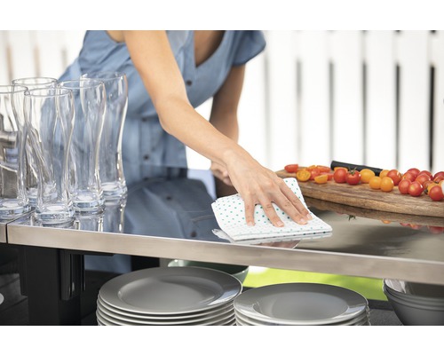 Žena utiera stôl utierkou, riad, poháre a paradajky na obrázku.