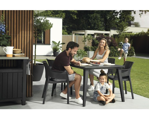 Rodina sedí vonku pri záhradnom stole so stoličkami.