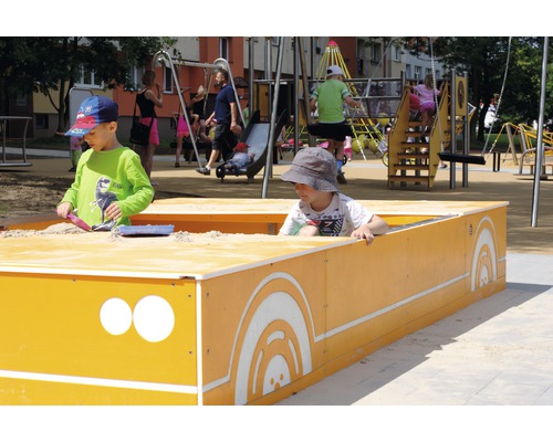 Dve deti sa hrajú v pieskovisku na ihrisku s hojdačkami a šmýkačkami.