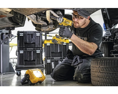 Mechanik pracuje s akumulátorovým rázovým uťahovákom na aute, v pozadí kufríky na náradie a pracovná lampa.
