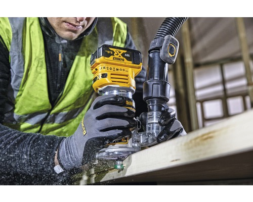 Muž frézuje drevenú dosku akumulátorovou hornou frézou. Pripojená je odsávacia hadica. Značka: DeWalt