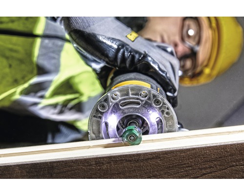 Detailný záber hornej frézky, ktorú obsluhuje osoba s ochrannou prilbou a rukavicami