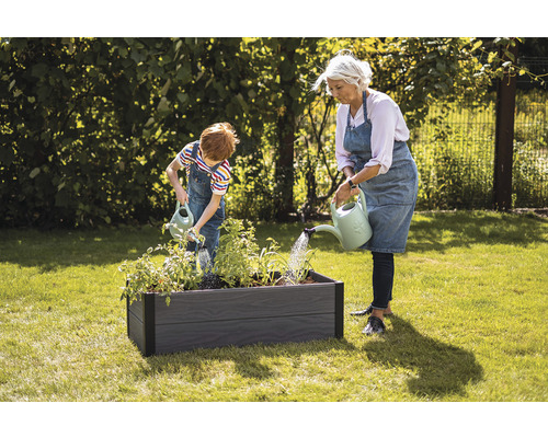 Žena a dieťa polievajú rastliny vo vyvýšenom záhone v záhrade.