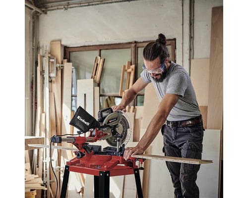 Muž používa pokosovú pílu Einhell na rezanie drevenej dosky v dielni.