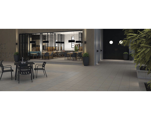 Vonkajší priestor reštaurácie s dlažobnými kockami, terénnymi úpravami a čiernymi stolmi so stoličkami.