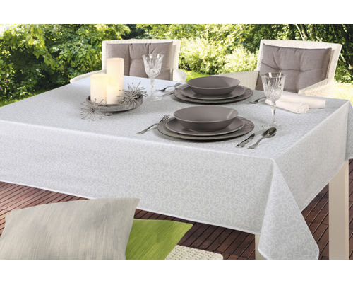 Prestretý záhradný stôl s bielym vzorovaným obrusom, riadom, pohármi a sviečkami