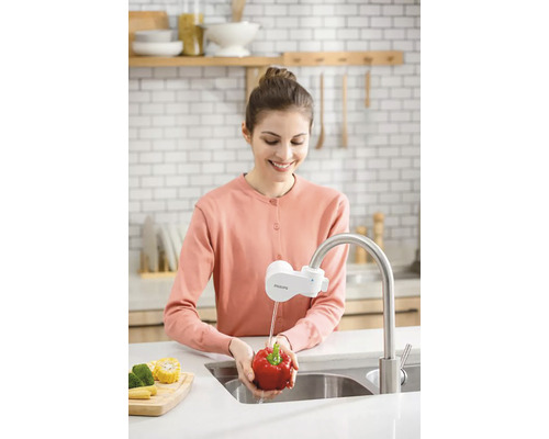 Žena umýva papriku pod vodovodným kohútikom s vodným filtrom v kuchyni.