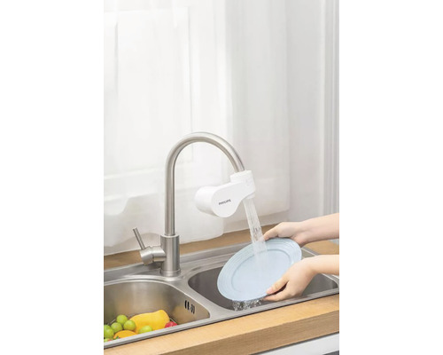 Kuchynská scéna s umývadlom, kohútikom s filtrom a rukami umývajúcimi tanier.