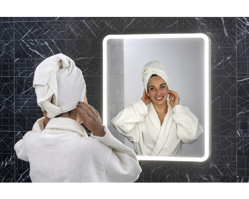 Žena s uterákom na hlave pred osvetleným kúpeľňovým zrkadlom