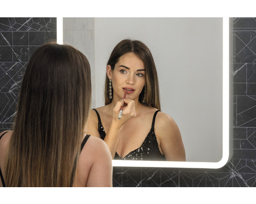 Žena sa líči rúžom pred osvetleným zrkadlom v kúpeľni