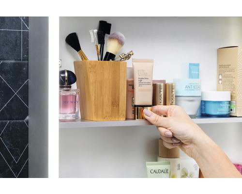 Kúpeľňová scéna s kozmetickými produktmi, štetcami na make-up v nádobe a rukou držiacou plechovku.