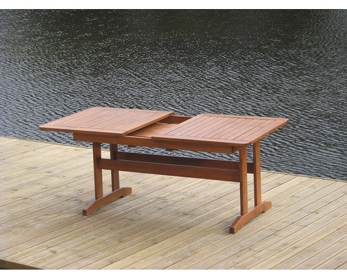 Rozkladací drevený záhradný stôl na drevenej terase s vodou v pozadí.