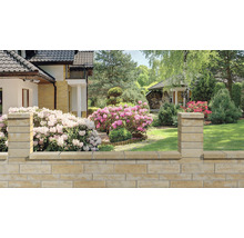 Kamenná záhradná stena s kvetmi a domom v pozadí