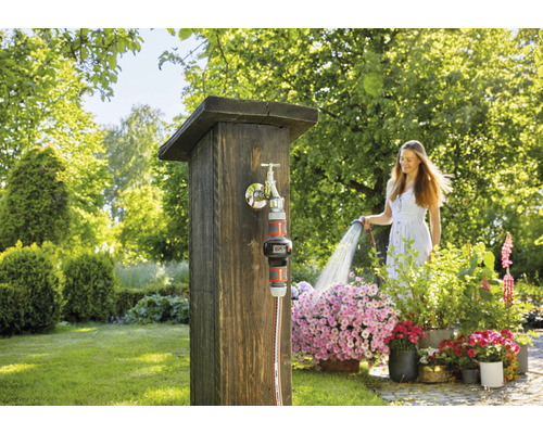 Žena polieva kvety záhradnou hadicou pri kohútiku v záhrade