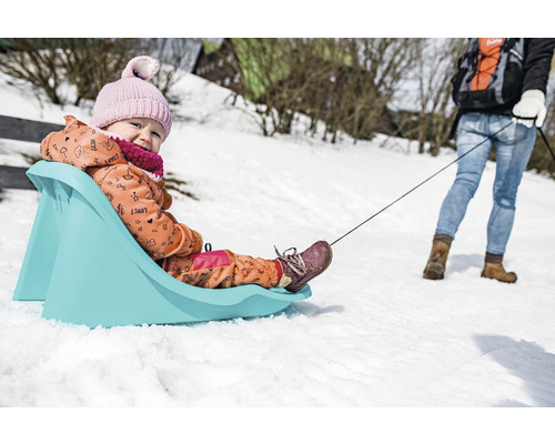 Dieťa na plastových saniach ťahá osoba v snehu
