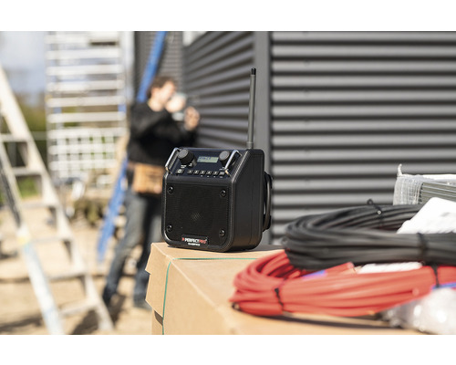 Stavebné rádio s anténou a káblemi a stavebný robotník v pozadí