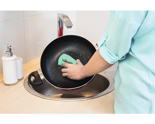 Osoba čistí panvicu hubkou na riad v dreze.