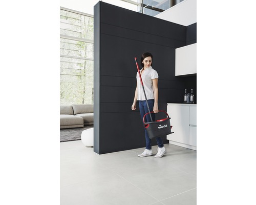 Žena nesie vedro a mop v modernom obývacom priestore.