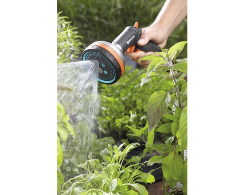 Ruka drží sprchovú hlavicu Gardena a zavlažuje rastliny.