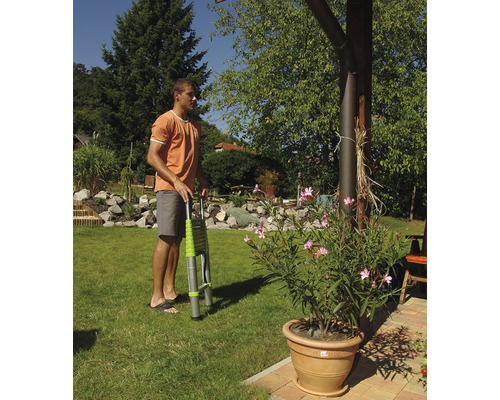 Muž drží teleskopický rebrík v záhrade.