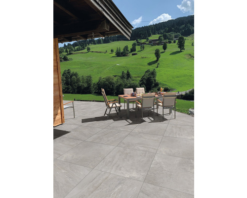 Keramická dlažba 60 x 120 x 2 cm Alpen Grigio Terasa so záhradným stolom a stoličkami pred zelenou krajinou.
