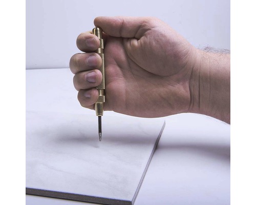 Ruka drží jamkovač nad dlaždicou