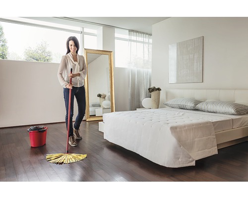 Žena vytiera drevenú podlahu mopom v spálni