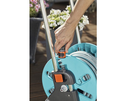 Osoba pripája záhradnú hadicu k hadicovému bubnu.