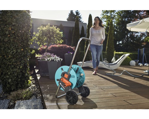 Navijak na hadicu Gardena na drevenej terase so ženou držiacou záhradnú hadicu