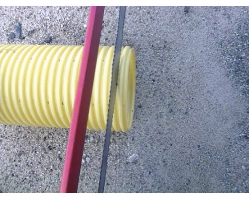 Žltá vlnitá rúrka sa reže pílkou na kov.