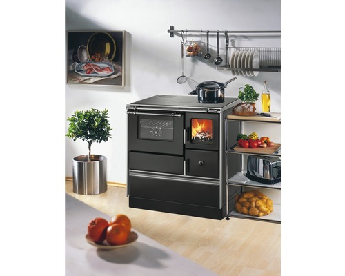 Kuchynská scéna s čiernym sporákom na drevo, hrncom, regálom a dekoratívnymi prvkami.