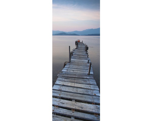 Dlhé staré drevené mólo vedie do vodnej plochy s horami v pozadí.