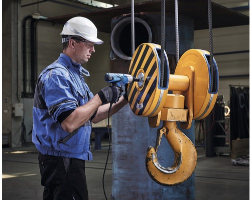 Muž s vŕtačkou na žeriavovom háku v dielni