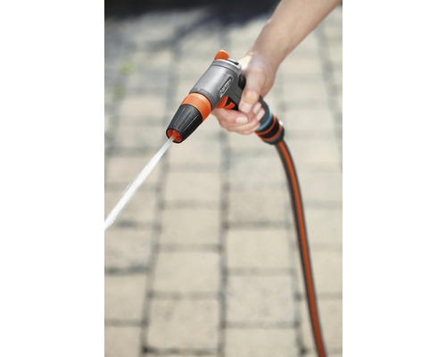 Ruka drží záhradnú striekaciu pištoľ s prúdom vody.