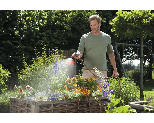 Muž zavlažuje kvety vo vyvýšenom záhone záhradnou hadicou