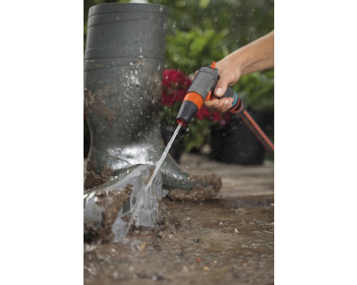 Osoba čistí záhradnú lopatu záhradnou sprchou vedľa gumákov.