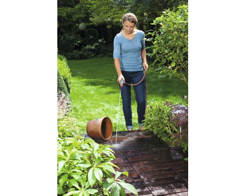 Žena zalieva hadicou terasu a kvetinovú vázu v záhrade.