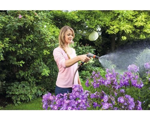 Žena polieva kvety záhradnou hadicou v záhrade.