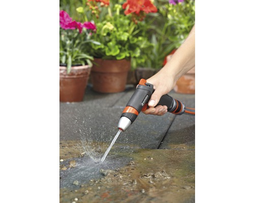 Osoba používa záhradnú striekaciu pištoľ na čistenie terasy pred osadenými kvetináčmi.