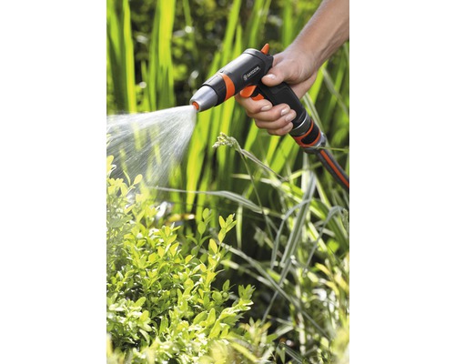 Ruka drží záhradný postrekovač, ktorý strieka vodu na rastliny.