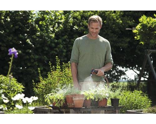 Muž zalieva rastliny v kvetináčoch záhradnou hadicou na záhrade.