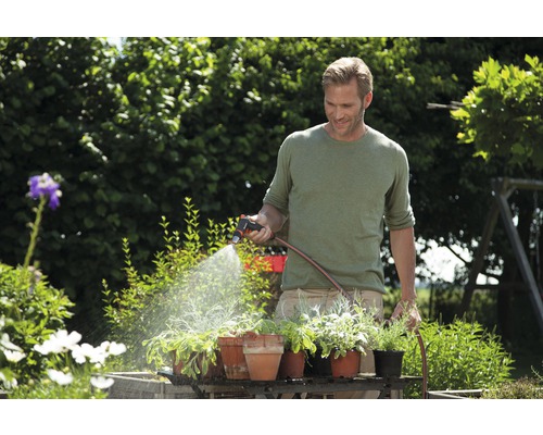 Muž zalieva rastliny v záhrade záhradnou striekačkou a záhradnou hadicou.