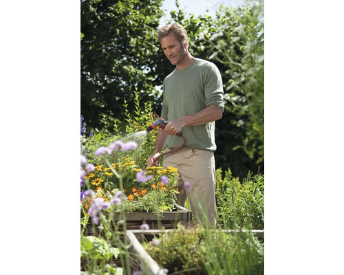 Muž zavlažuje kvety záhradnou hadicou v záhrade.