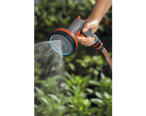 Osoba drží viacúčelovú záhradnú striekaciu pištoľ Gardena, ktorá strieka vodu.